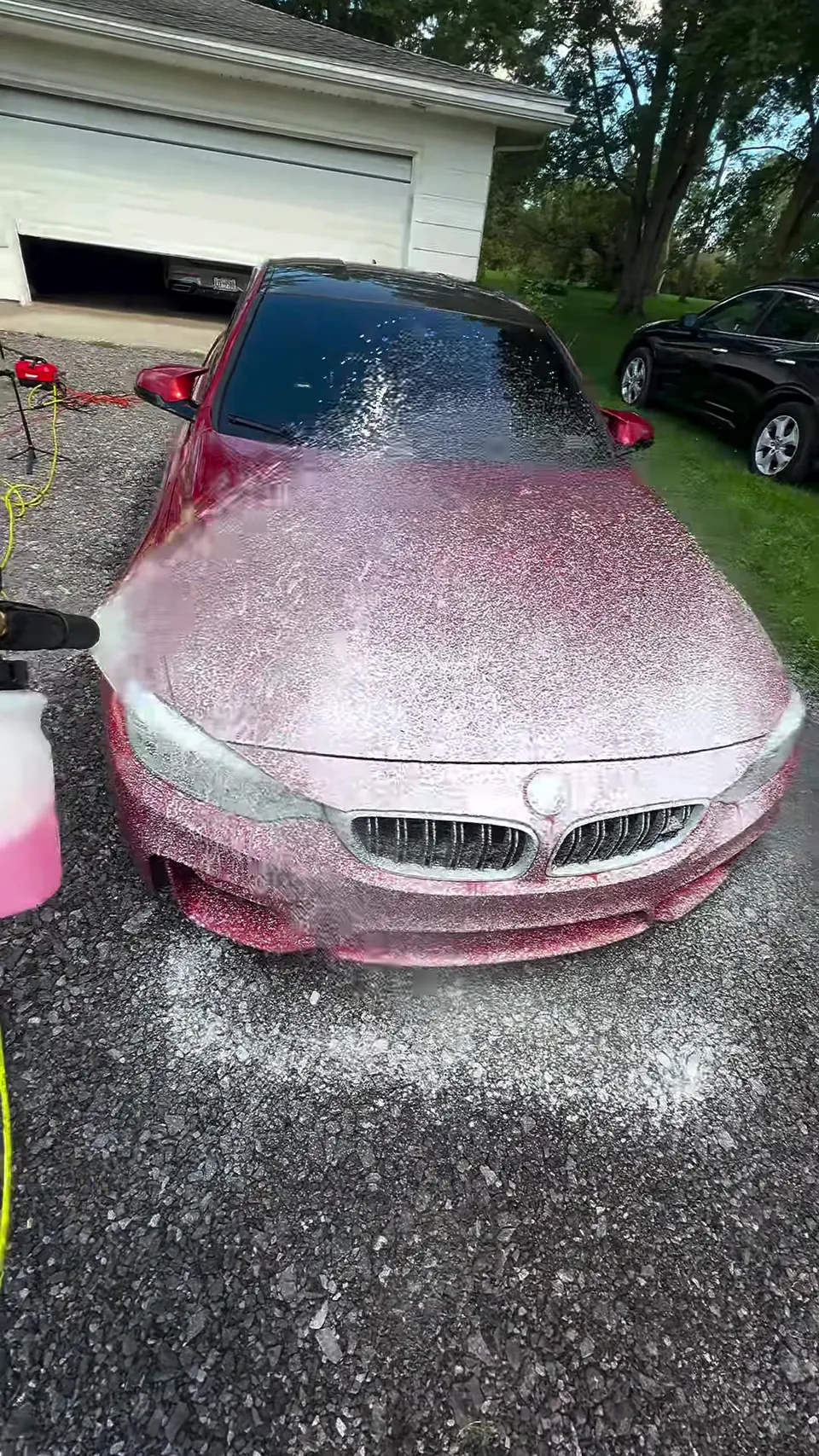 Red BMW M4 being covered in foam during a foam wash on a gravel driveway