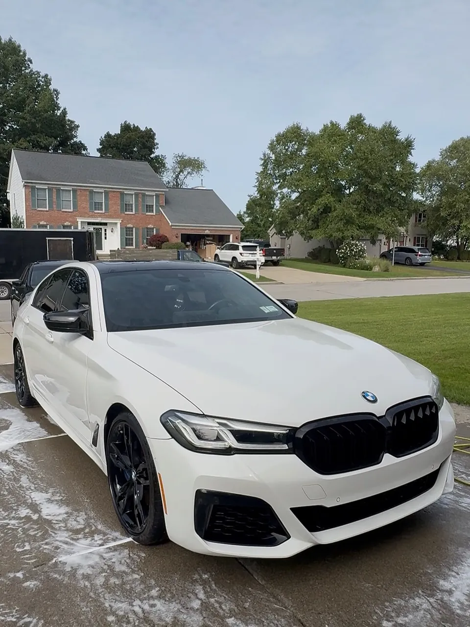 White BMW M550i being washed on a residential driveway during a mobile detail