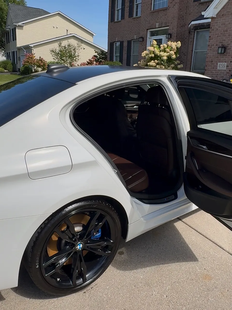 White BMW M550i with doors open showing its brown leather interior after a full detail